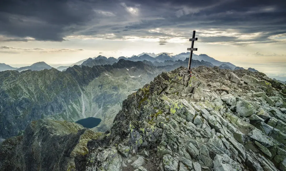 Szczyt Tatr z krzyżem, kamienista ścieżka, jezioro w dole. Krywań trudność pokonana, widok zapiera dech.