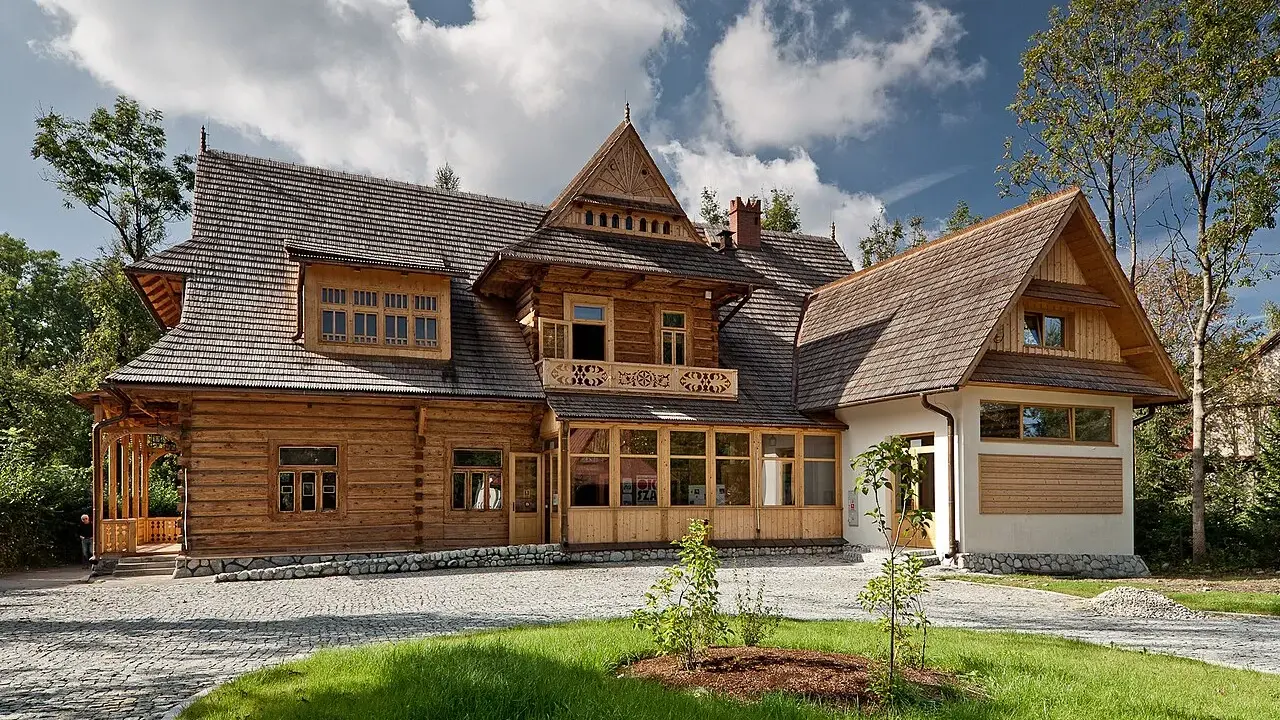 Drewniany dom w stylu zakopiańskim, z charakterystyczną zakopiańską architekturą, ozdobnymi detalami i kamienną podmurówką.