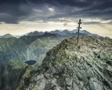 Szczyt Tatr z krzyżem, kamienista ścieżka, jezioro w dole. Krywań trudność pokonana, widok zapiera dech.