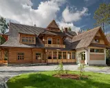 Drewniany dom w stylu zakopiańskim, z charakterystyczną zakopiańską architekturą, ozdobnymi detalami i kamienną podmurówką.