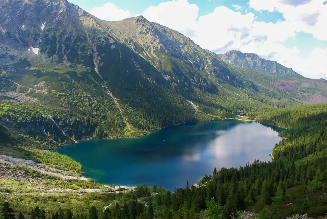 Malowniczy widok na Morskie Oko, gdzie szlak turystyczny wije się wśród zielonych zboczy Tatr.