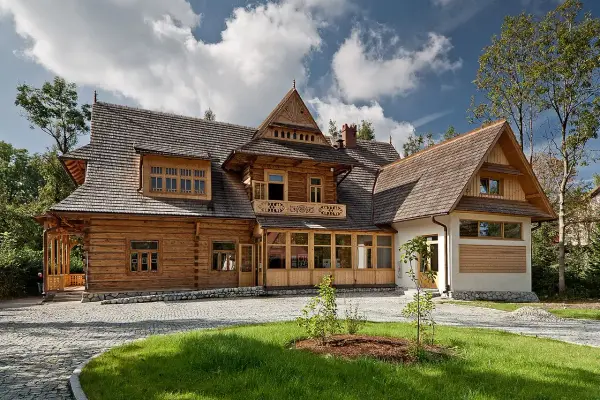 Drewniany dom w stylu zakopiańskim, z charakterystyczną zakopiańską architekturą, ozdobnymi detalami i kamienną podmurówką.